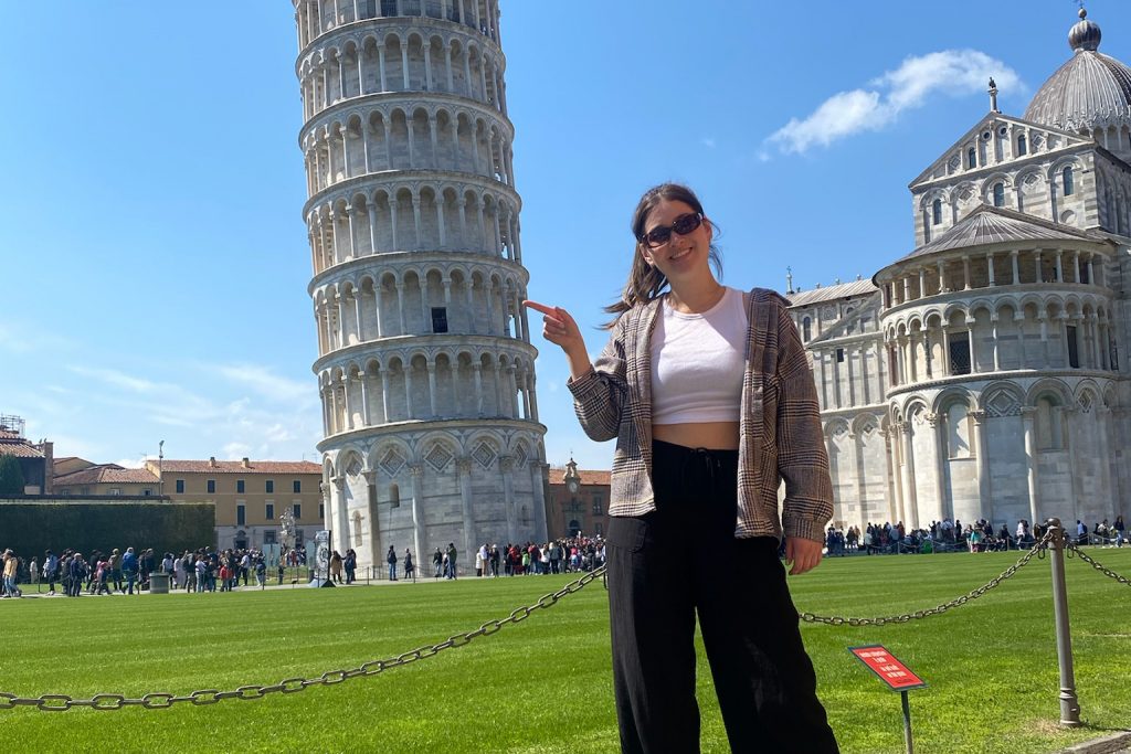 young woman smiling in front of tower of pisa italy